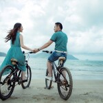young couple on bicycle holding hands, beach side